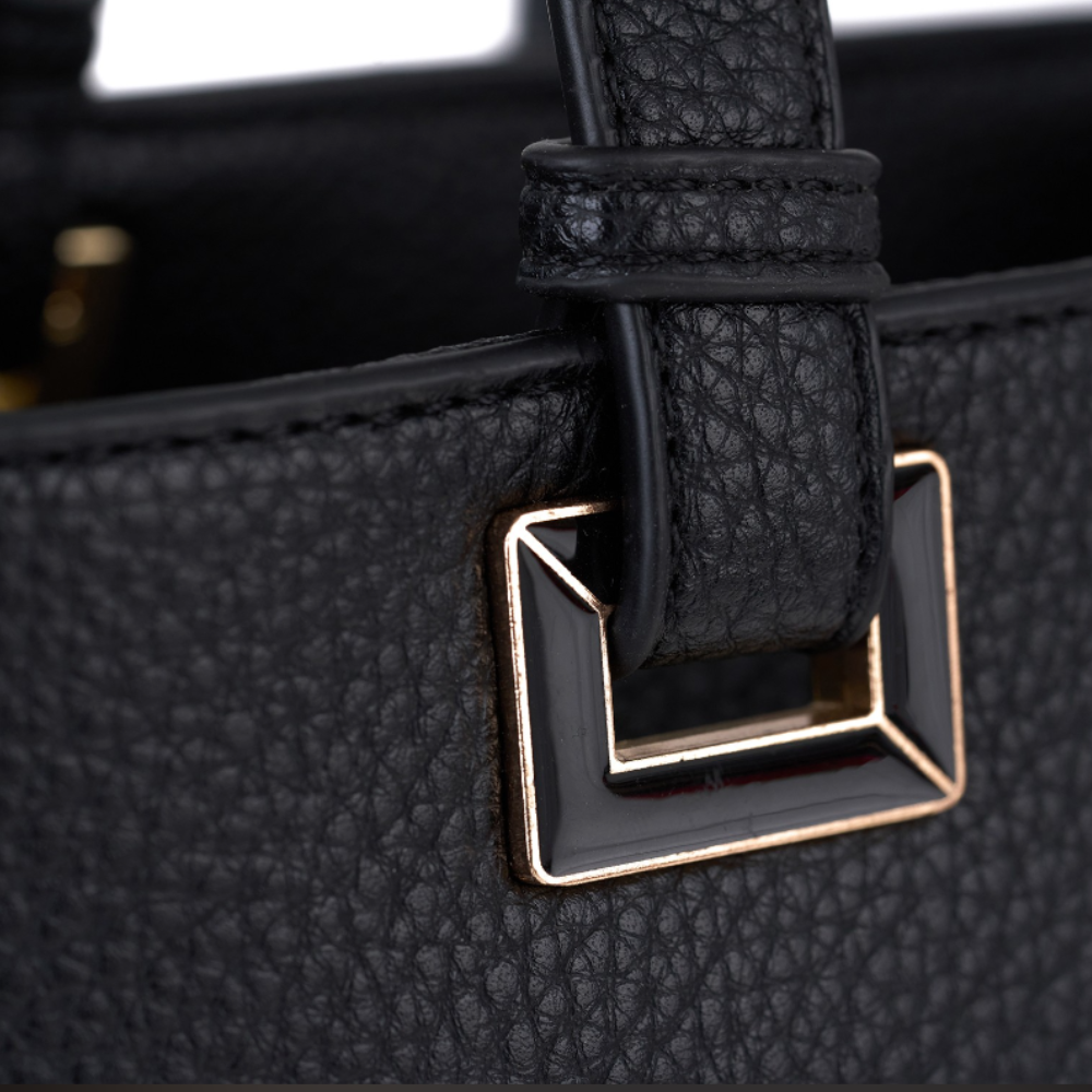 Close-up of a black pebbled leather handbag showing a strap attached to a geometric gold-tone metal hardware detail.