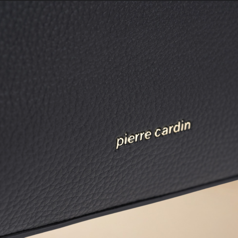 Close-up of a black textured leather item with the 'pierre cardin' logo in gold lettering, set against a neutral beige background.