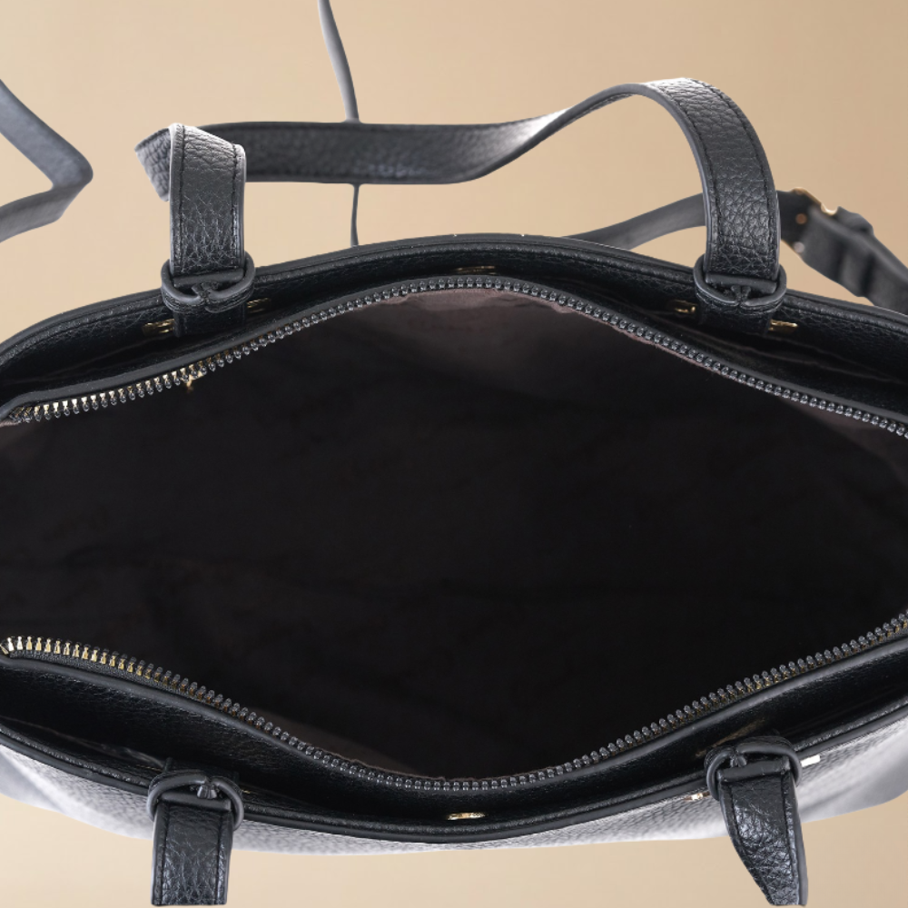 Close-up of the interior of a black textured leather handbag, showing the open zippered compartment, black lining, and part of the strap against a warm beige background.