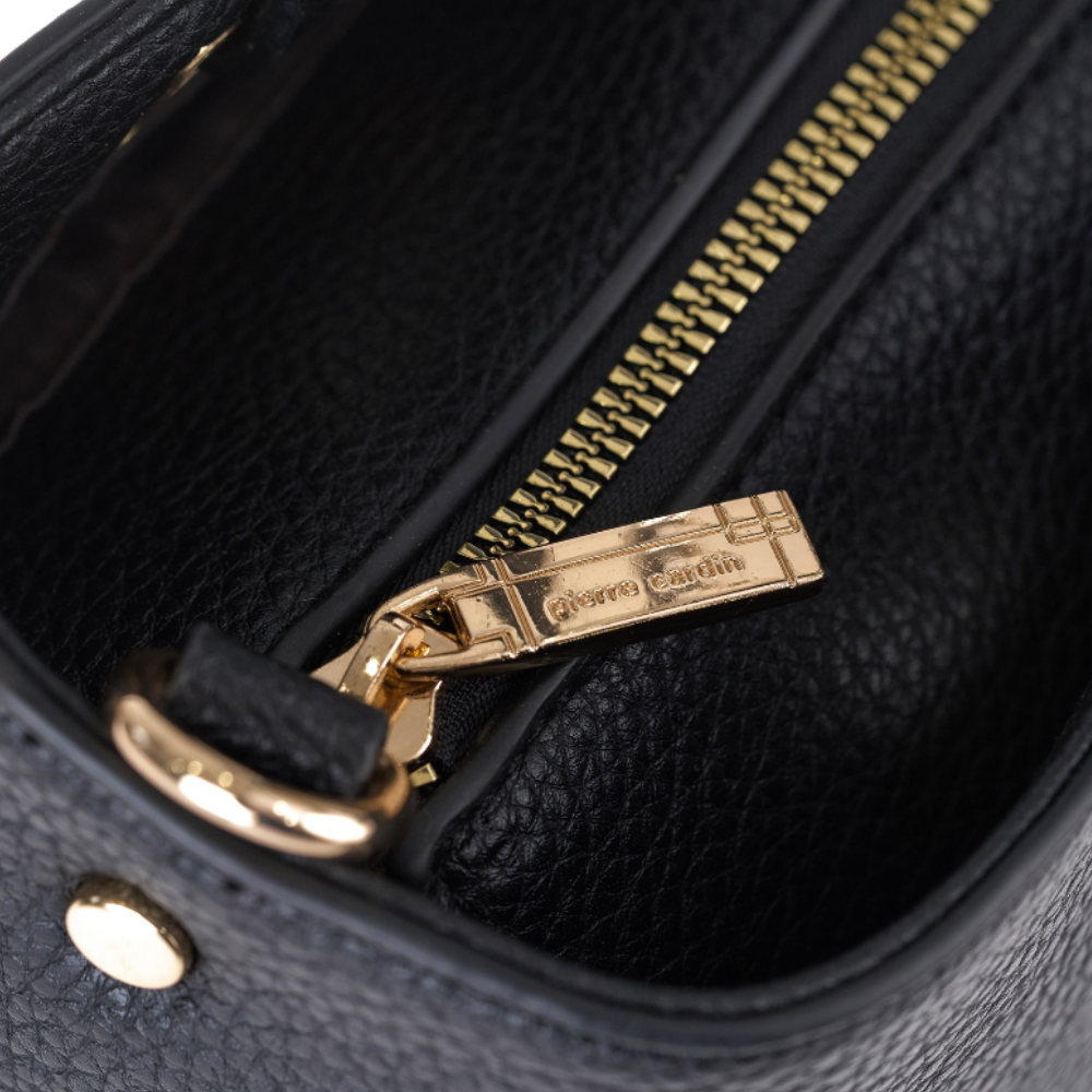Close-up of a black pebbled leather bag interior showing a gold-tone zipper with a branded pull tab that reads 'Pierre Cardin'.