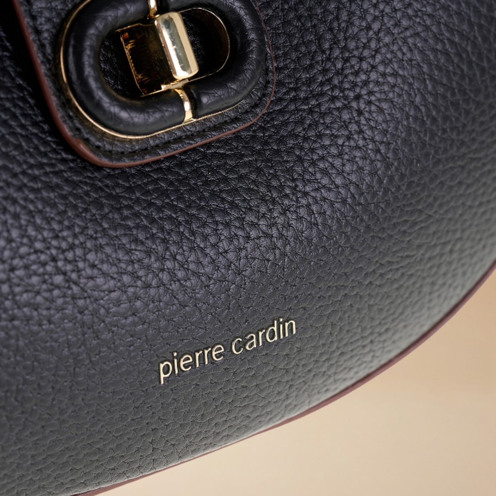 Close-up of a black pebbled leather handbag by Pierre Cardin, showing a gold-tone metal D-ring closure and the gold-embossed 'pierre cardin' logo on the side.