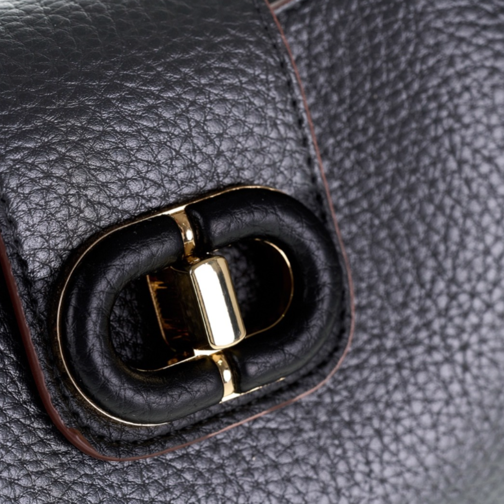 Close-up of a black pebbled leather bag with a large gold-tone metal O-ring closure and black leather trim.
