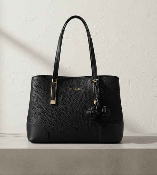 Black handbag on a light gray pedestal against a white textured wall.