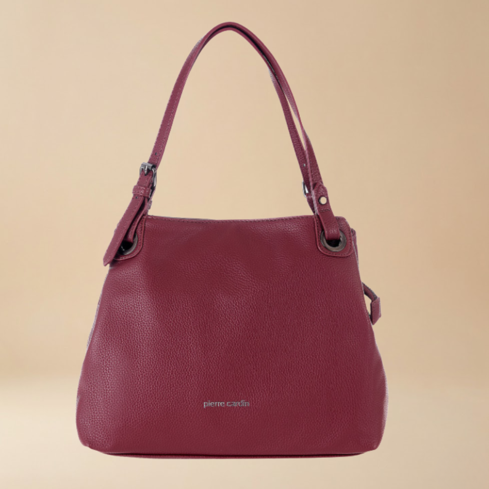 A burgundy pebbled leather shoulder bag by Pierre Cardis, featuring dual top handles, metal hardware, and a small silver brand logo on the front, set against a solid beige background.