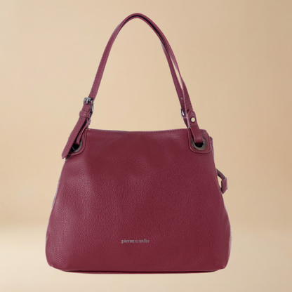 A burgundy pebbled leather shoulder bag by Pierre Cardis, featuring dual top handles, metal hardware, and a small silver brand logo on the front, set against a solid beige background.